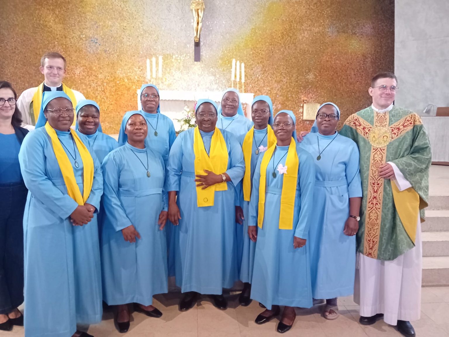 Les sœurs, écharpe jaune sur l’habit bleu, entourées de deux prêtres devant l’autel lors de la messe d’installation
